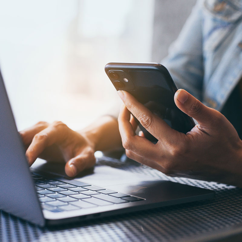 Photo of person working at computer and holding cellphone